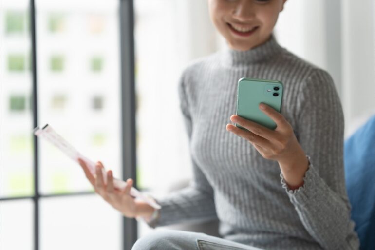 woman on her phone holding a checking account statement and smiling.