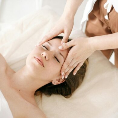 A licensed skincare professional performing a facial treatment on a relaxed woman lying on a treatment table at a medical aesthetic clinic, with gentle hand placement on her forehead in a clean, softly lit spa environment.