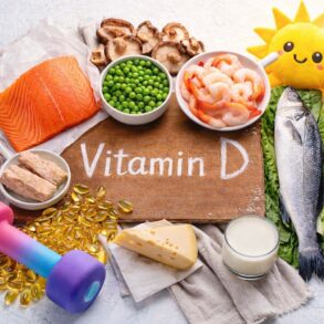 Overhead photo of vitamin D foods and fitness items arranged on a light background. In the center is a wooden board with the words ‘Vitamin D’ written on it. Around the board are salmon, a whole fish, shrimp, eggs, mushrooms, green peas, cheese, butter, and a glass of milk. Nearby are yellow vitamin D gel capsules and a colorful dumbbell representing exercise and muscle building. A small plush sun toy appears in the corner to represent sunlight as a source of vitamin D.