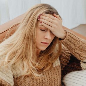 a woman on her couch with a hand on her head having brain fog