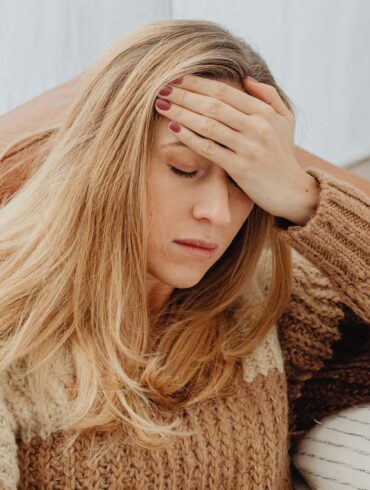 a woman on her couch with a hand on her head having brain fog