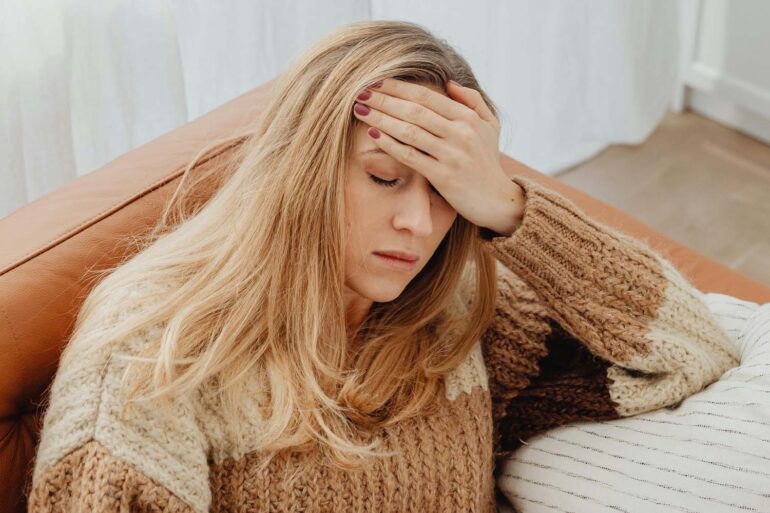 a woman on her couch with a hand on her head having brain fog