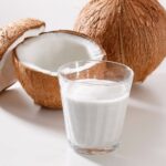 a glass of coconut milk next to an open coconut and a whole one.