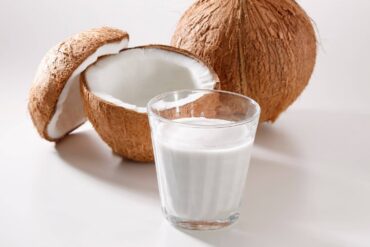 a glass of coconut milk next to an open coconut and a whole one.