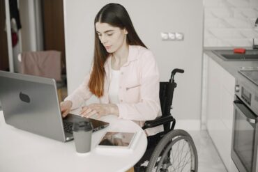 Woman in a wheelchair using a laptop at a kitchen counter in an accessible home
