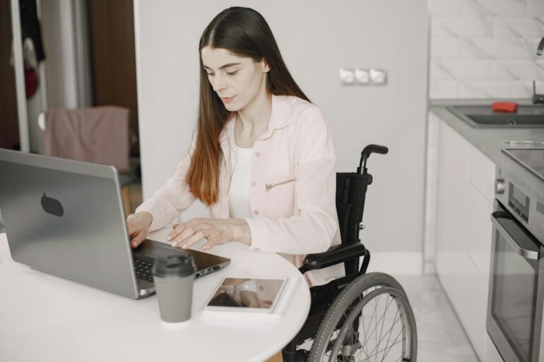 Woman in a wheelchair using a laptop at a kitchen counter in an accessible home