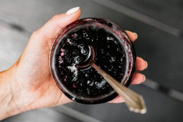 a woman holding an open jar of jelly with a spoon in it.