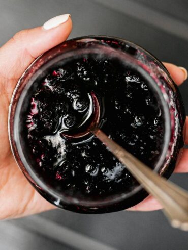 a woman holding an open jar of jelly with a spoon in it.