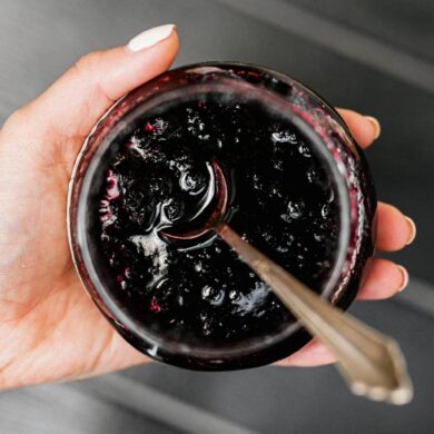 a woman holding an open jar of jelly with a spoon in it.