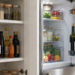 Cooking wine bottle on a pantry shelf at room temperature next to condiments, with an open fridge in the background holding a corked red wine and a bottle of Marsala