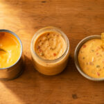 an open can of nacho cheese sauce with a spoon. Center: a jar of Tostitos queso with the lid off. Right: a small bowl of homemade queso with a chip resting on the edge