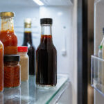 A bottle of ponzu sauce on a refrigerator shelf between other Asian condiment bottles, door slightly open