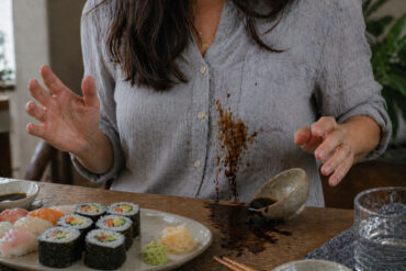 A woman eating sushi and splashing soy sauce on her shirt as the bowl is tipped