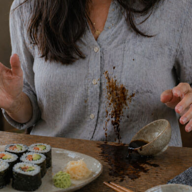 A woman eating sushi and splashing soy sauce on her shirt as the bowl is tipped