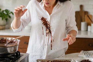 Close-up of a person in a white linen shirt with melted chocolate spilled down the front while working over a double boiler in a kitchen