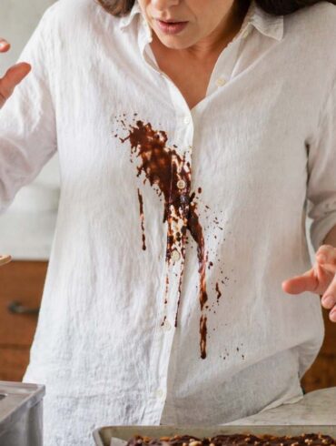 Close-up of a person in a white linen shirt with melted chocolate spilled down the front while working over a double boiler in a kitchen