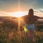 Woman Stands on Mountain over Field Under Cloudy Sky at Sunrise