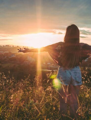 Woman Stands on Mountain over Field Under Cloudy Sky at Sunrise