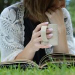 a woman with a mug using simply thick while reading a book in the grass