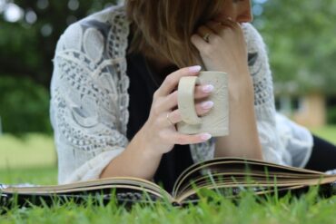 a woman with a mug using simply thick while reading a book in the grass