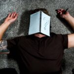 A person with Unspecified-Neurodevelopmental-Disorder-UNDD laying on the ground with a notebook that has a question mark written on it.
