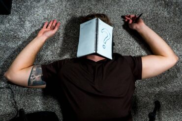 A person with Unspecified-Neurodevelopmental-Disorder-UNDD laying on the ground with a notebook that has a question mark written on it.