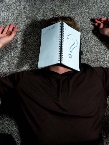 A person with Unspecified-Neurodevelopmental-Disorder-UNDD laying on the ground with a notebook that has a question mark written on it.