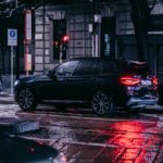 A nighttime street scene in the city featuring a car with 23565R17 all-season tires on a wet, rainy night surrounded by urban lights.