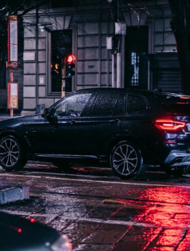 A nighttime street scene in the city featuring a car with 23565R17 all-season tires on a wet, rainy night surrounded by urban lights.