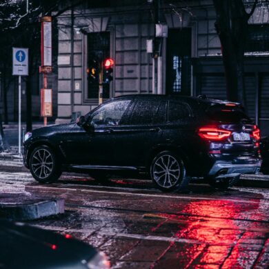 A nighttime street scene in the city featuring a car with 23565R17 all-season tires on a wet, rainy night surrounded by urban lights.