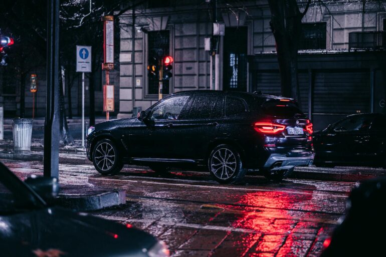 A nighttime street scene in the city featuring a car with 23565R17 all-season tires on a wet, rainy night surrounded by urban lights.