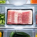 a sealed package of raw bacon sitting upright on a middle refrigerator interior shelf