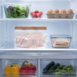 an open refrigerator interior. A sealed package of deli turkey sits naturally on the middle interior shelf, centered in frame. A small airtight glass container of sliced turkey sits beside it.