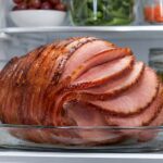 a sliced spiral ham on the shelf of an open fridge