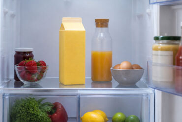 Eye-level shot of an open refrigerator interior. A quart carton of buttermilk stands upright on the middle interior shelf, centered in frame