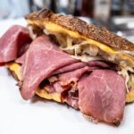 Close-up of a flavorful pastrami sandwich with cheese and sauerkraut on rustic bread
