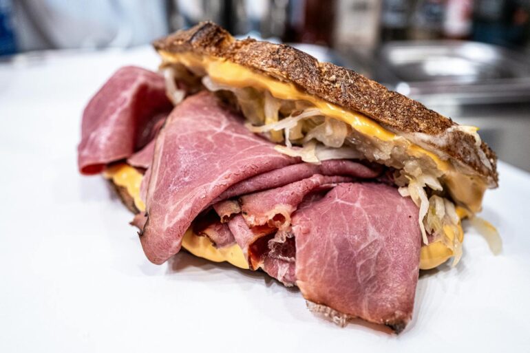 Close-up of a flavorful pastrami sandwich with cheese and sauerkraut on rustic bread