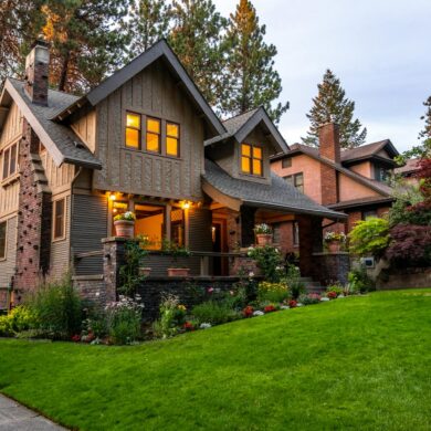 A beautifully lit Victorian-style house surrounded by a lush garden at twilight, showcasing classic architecture.