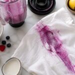 a large berry stain on a white shirt from a blender spill on a counter with cleaning supplies