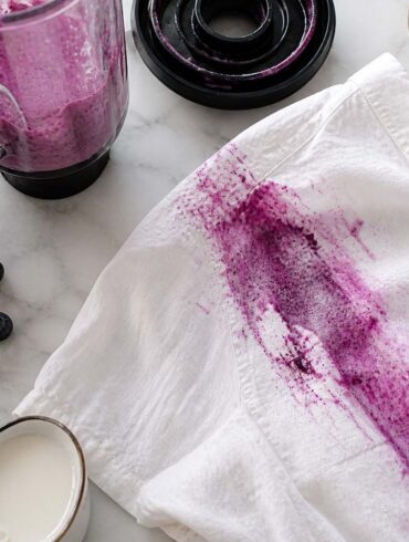 a large berry stain on a white shirt from a blender spill on a counter with cleaning supplies
