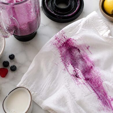 a large berry stain on a white shirt from a blender spill on a counter with cleaning supplies