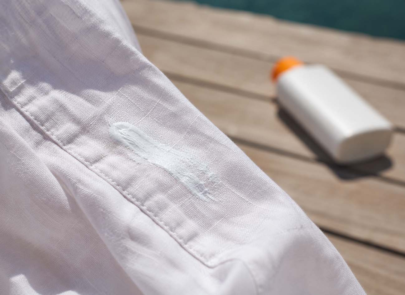 a white linen shirt stained with sunscreen on a deck next to the opened bottle
