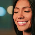 Close-up portrait of a woman with Invisalign smiling with eyes closed, in soft focus lighting