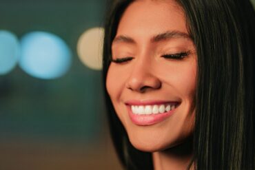 Close-up portrait of a woman with Invisalign smiling with eyes closed, in soft focus lighting