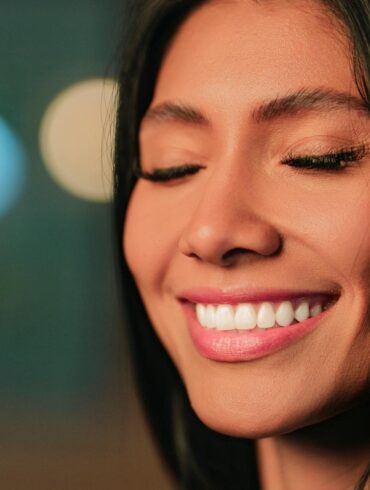 Close-up portrait of a woman with Invisalign smiling with eyes closed, in soft focus lighting