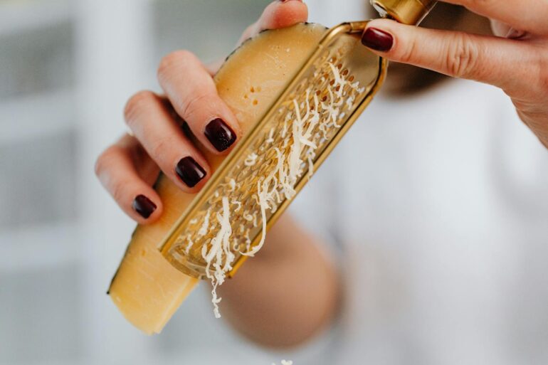 Close-up image of grated parmesan cheese with focus on hands and food preparation.