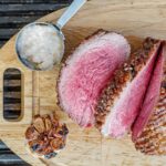 a whole sliced roast beef ona cutting board with garlic and horseradish sauce