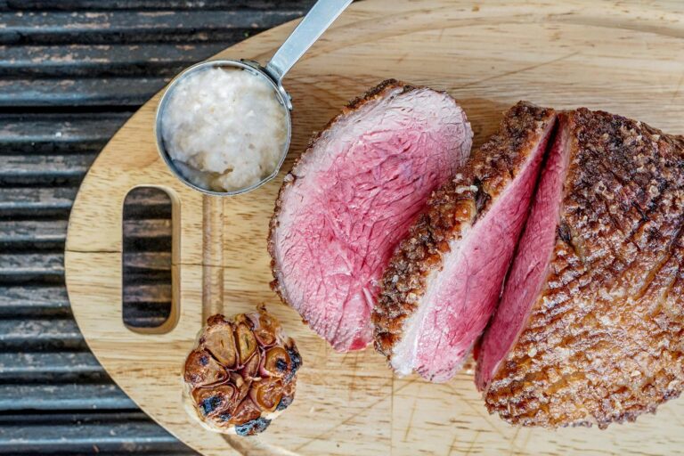 a whole sliced roast beef ona cutting board with garlic and horseradish sauce