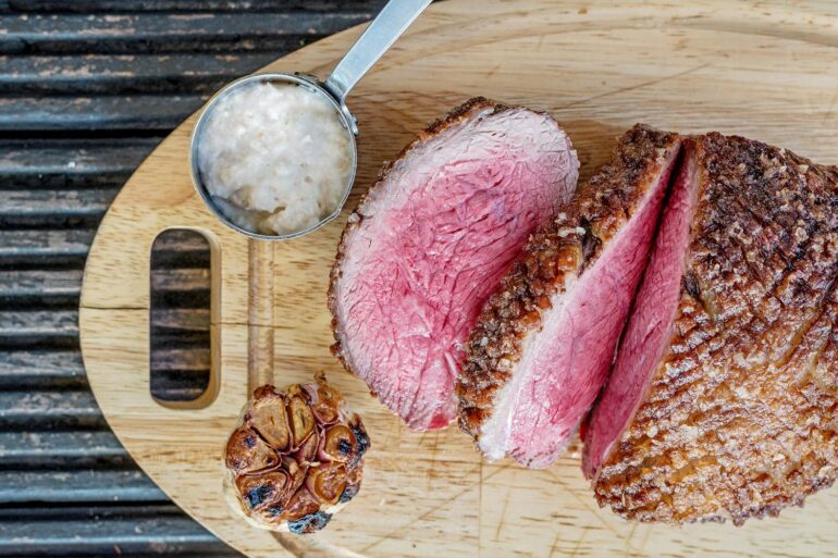 a whole sliced roast beef ona cutting board with garlic and horseradish sauce