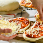 a bowl of shredded cheese with someone using it to make mini pizzas